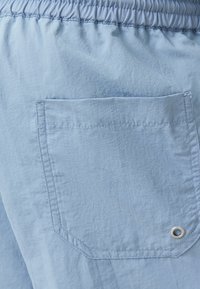 Pantalones cortos de color azul claro con cintura elástica, que cuentan con un bolsillo trasero de forma rectangular y un detalle de ojete de metal. Textura suave.