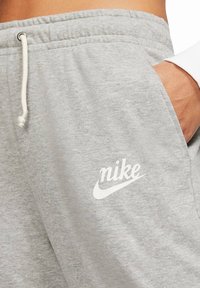 Šedé tepláky z bavlněné směsové látky s šňůrkou v pase a bílým logem Nike na přední straně. Měkká textura.