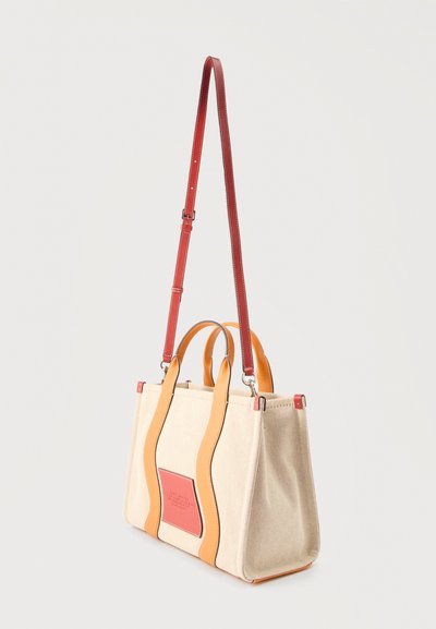 Μπεζ τσάντα καμβά με πορτοκαλί κάθετους ιμάντες, κόκκινο ρυθμιζόμενο ιμάντα ώμου και μικρό κόκκινο μπροστινό διακοσμητικό.