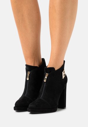 Bottines en daim noir à talon carré haut, avec fermetures éclair dorées et un accent décoratif doré sur le côté.