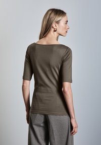 Oliwkowa dopasowana koszulka z okrągłym dekoltem i krótkimi rękawami, wykonana z gładkiego materiału; zestawiona z szerokimi spodniami w kratę.