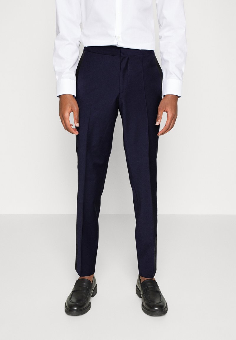 Marineblauwe pantalon met een gladde textuur, voorzien van een platte voorkant en een rechte pijp, gecombineerd met zwarte instappers.