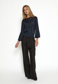 Námornícka trblietavá blúzka s dlhým rukávom a voľným strihom, skombinovaná s vysokými čiernymi nohavicami s širokými nohavicami. Hladká látka s jemným leskom.