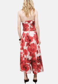 Strapless floral dress featuring a red and white pattern, flowy fabric, waist belt, and ankle-length cut. Smooth texture.
