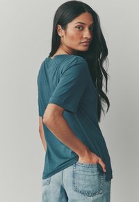 Teal värvi lühikeste varrukatega T-särk, lõdva lõikega, ümarate kaelustega ja sileda tekstuuriga, koos teksapükstega. Minimalistlik disain, ilma mustriteta.