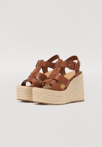 Sandali wedge in pelle marrone con cinturini incrociati, dotati di una piattaforma in espadrillas beige testurizzata e fibbia regolabile.
