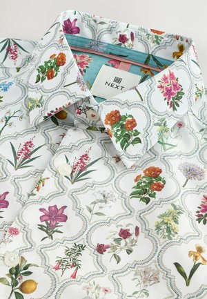 Camisa blanca con botones con un estampado floral en varios colores, con un cuello estampado y detalles de botones. Etiqueta de la marca visible en el interior.
