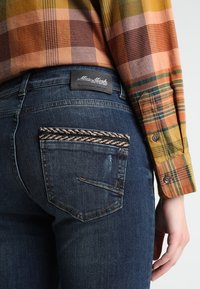 Mörkblå jeans med en udemärkt vävd accent på bakfickan; har en varumärkesetikett vid midjan och subtila blekningsdetaljer.