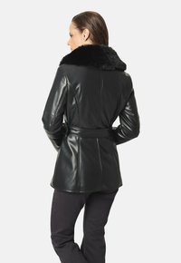 Chaqueta de cuero negra con cuello de piel sintética, cintura ceñida con cinturón y corte entallado. Textura elegante y detalles de costura visibles.