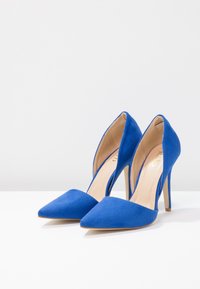 Chaussures à talons hauts en daim bleu avec un design à bout pointu et des côtés découpés. Doublure intérieure beige clair et un talon aiguille fin.