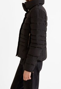 Černá péřová bunda s prošívanými částmi, vysokým límcem a kapsami na zip. Vyrobena z lehkého, voděodolného materiálu.
