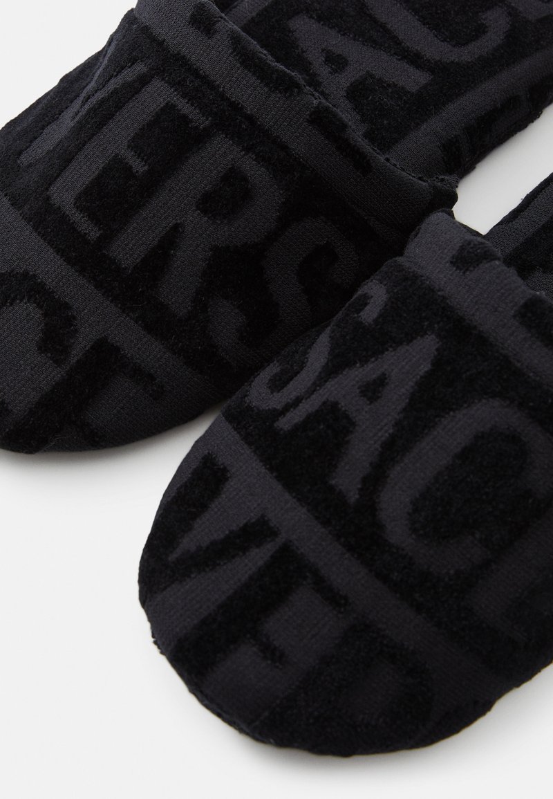 Sorte slippers med en blød tekstur og præget tekstmønster, der har en rund tå og lavprofil design. Materialet ser blødt og behageligt ud.