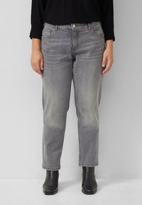 Jeans en denim gris avec une coupe décontractée, une texture décolorée, cinq poches et une fermeture à boutons. Associés à des bottines noires.