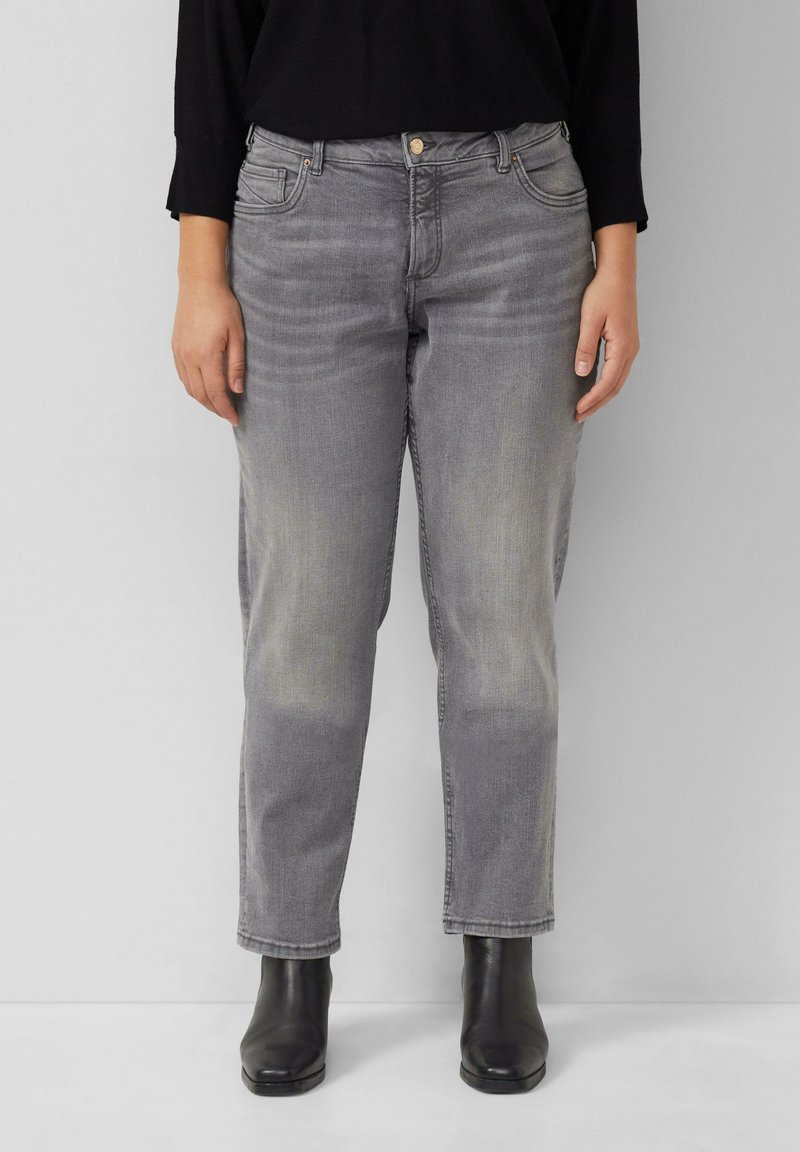 Jeans en denim gris avec une coupe décontractée, une texture décolorée, cinq poches et une fermeture à boutons. Associés à des bottines noires.