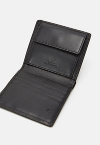 Portafoglio in pelle nera con svariati scomparti per carte, una tasca a pattina e un branding discreto. La texture liscia e i bordi cuciti esaltano il design.