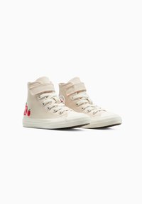 Canvas hoge sneakers in lichtroze met witte rubberen zolen en neusstukken. Voorzien van rode appelborduursels en twee verstelbare klittenbandsluitingen.