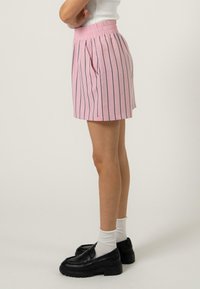 Shorts roses avec des rayures verticales marine, taille élastique, poches latérales et coupe ample. Associés à des chaussures noires à enfiler et des chaussettes blanches.