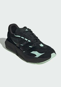 Sort atletisk sko med et mesh-design, mintgrønne accenter, teksturerede overlays og en tykk, vinkelret sål. Snøret med sorte snørebånd.