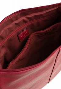 Interno di una borsa a tracolla rossa in pelle con una superficie liscia, caratterizzato da più scomparti e una tasca con zip. L'imbottitura è in un tessuto di un rosso più scuro.