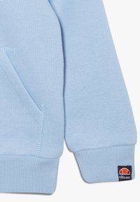 Sweat-shirt bleu clair avec poignets et ourlet côtelés. Comprend une poche avant et une petite étiquette logo en orange, rouge et marine sur la manche.