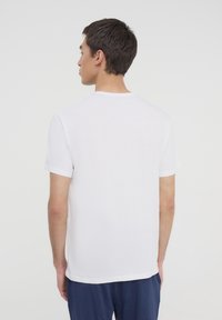 T-shirt bianco in cotone con colletto rotondo e maniche corte, caratterizzato da un retro semplice senza disegni o logo. Tessuto morbido.