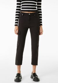 Svarta cargo-byxor med sidfickor, kortad nederkant och fransade kanter, i kombination med en svart och vit randig långärmad topp och svarta skor.