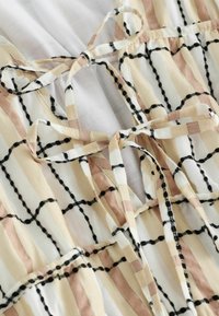 Top de tela ligera con un patrón de cuadrícula en beige, blanco y negro, con tirantes atados y una textura suave.