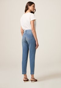 Jeans de un azul claro con cintura alta, perneras ajustadas y bolsillos traseros. Combinados con una blusa blanca de manga corta y sandalias de tacón marrones.