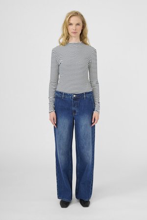 Melnā un baltā svītrainā garām piedurknēm krekls, kombinēts ar platajām zilajām denim biksēm. Gluda tekstūra, standarta josta un priekšējā pogu detaļa.