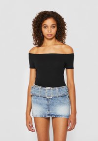 Top negru, cu umerii goi, purtat cu o fustă mini din denim albastru decolorat, cu talie largă și curea cu cataramă argintie.