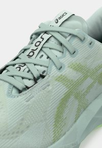 Scarpa sportiva azzurro chiaro con tomaia in rete testurizzata, lacci tonali e un motivo verde lime. Presenta il logo sulla linguetta e sulla suola.