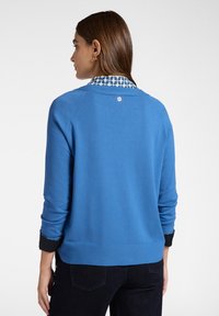 Maglione blu lavorato a maglia con scollatura rotonda, dotato di un colletto decorato, polsi neri e un piccolo logo sul retro. Vestibilità classica e texture morbida.