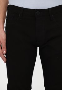 Jeans in denim nero con una vestibilità slim, caratterizzati da una chiusura con bottone frontale, due tasche laterali e cuciture tono su tono.