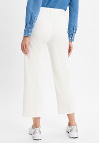 Weiße, weit geschnittene Hosen mit glatter Textur, einer Gesäßtasche und umgeschlagenem Saum, kombiniert mit grauen Sportschuhen und einem Jeanshemd.