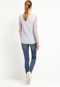 Vaaleansininen, tekstuuroitu paita, jossa on kolmivartiset verkkohihat, yhdistettyinä saumoihin istuviin sinisiin farkkuihin ja valkoisiin lenkkareihin, näkymä takaa.