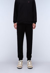 Zwarte sweatshirt en broek van zachte stof met geribbelde boorden. Schoenen met een beige en witte uitvoering, voorzien van veters en een gestructureerde zool.