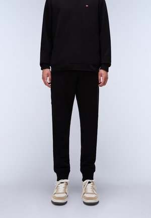 Black sweatshirt and pants made of soft fabric with ribbed cuffs. Shoes feature a beige and white design with laces and a textured sole.