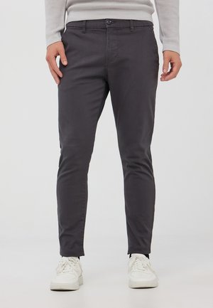 Pantaloni slim-fit grigio scuro realizzati in tessuto misto cotone, con chiusura a bottoncino, passanti per cintura e tasche frontali. Abbinati a sneakers bianche.