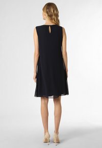 Robe sans manches de couleur marine avec un dos en forme de trou de serrure, fabriquée dans un tissu léger, présentant une texture lisse et une silhouette fluide.