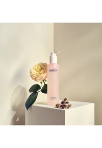 Babor Soothing Rose Toner i en frostad rosa flaska med en vit pump, tillsammans med en blek ros och gröna blad på en ljus bakgrund.