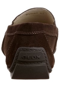 Brune ruskinds slip-ons med en struktureret gummisål, som har subtil syning og et logo på hælen. Enkel design, lav profil.