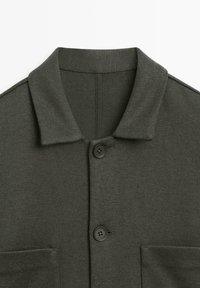 Cappotto in misto lana verde scuro con una texture morbida, colletto a risvolto, chiusura frontale con bottoni e due tasche anteriori.