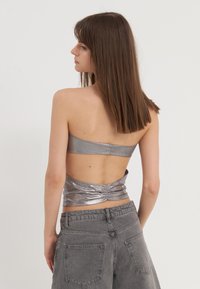 Metallik hõbedane õlgadeta crop top, millel on volangidega seljaosa. Kombineeritud kõrge vöökohaga, hõbenahksest hallidest teksadest. Sile, läikiv tekstuur.