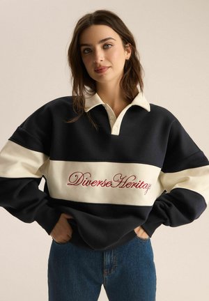 Granatowy i kremowy sweatshirt z kołnierzykiem polo, z haftem "Diverse Heritage" na czerwono na klatce piersiowej. Miękki, gruby materiał.