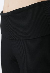 Leggings noirs côtelés avec une large taille, présentant une surface texturée et une coupe ajustée. Le matériau semble extensible et lisse.