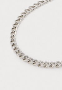 Primo piano di una collana con catena in argento lucido su uno sfondo bianco semplice.