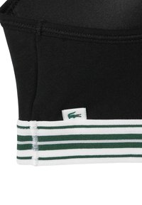 Sujeción deportiva negra con banda elástica a rayas verdes y blancas; cuenta con una pequeña etiqueta de logo con el emblema de un cocodrilo. Textura suave, diseño sin costuras.
