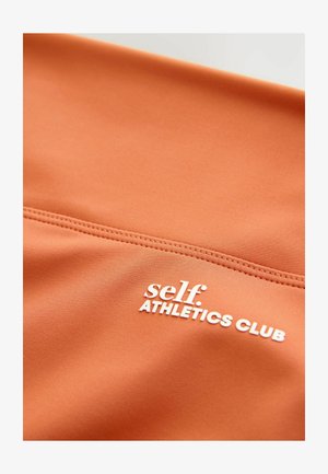Tissu de sport orange au toucher lisse, avec du texte blanc "self. ATHLETICS CLUB" et un détail de couture.