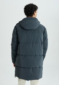 Mørkegrå pufferjakke med hætte, der har et quiltet design og elastiske snore nederst. Glat, vandafvisende materiale.