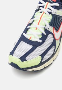 Sportovní bota s vrchní částí z prodyšné síťoviny a syntetického materiálu v námořnické modré, bílé a neonově zelené, s kontrastními akcenty, tkaničkami a polstrovanou podrážkou.